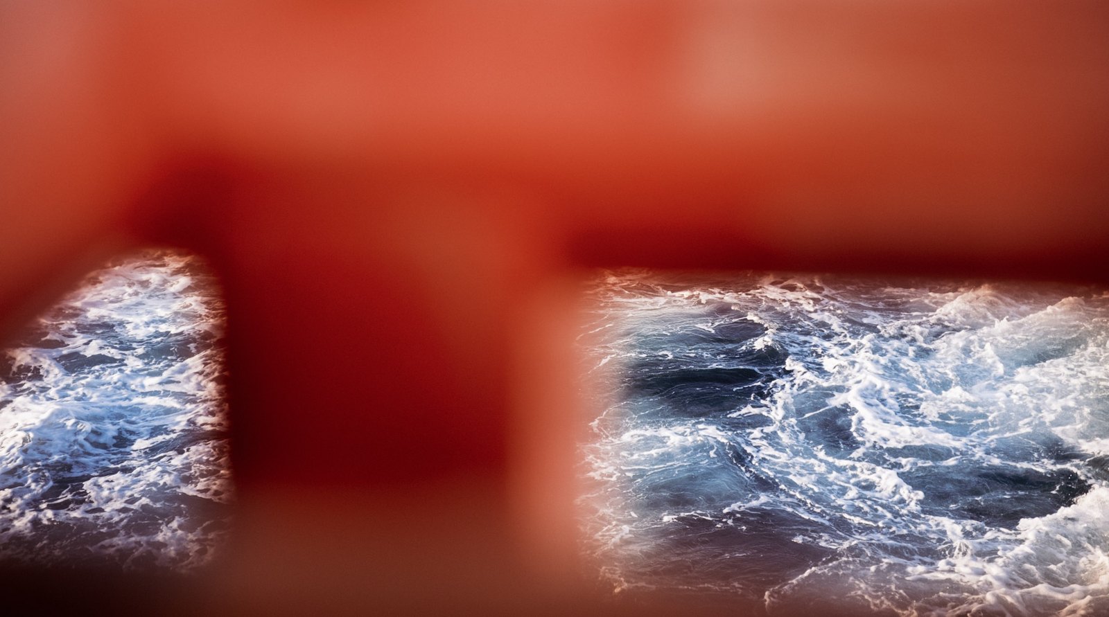 Red Veil: a red railing out of focus before the surf.
