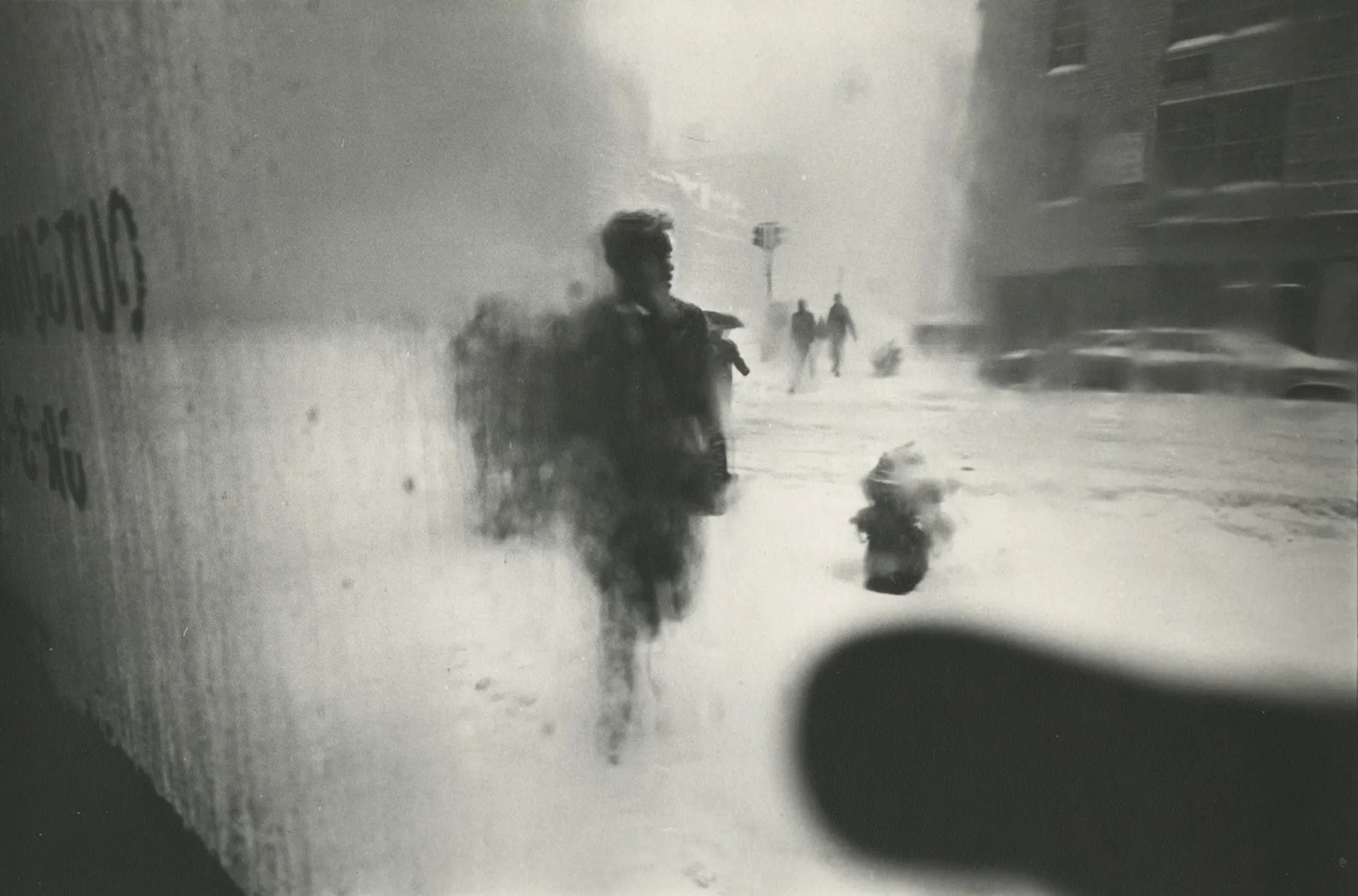 A snowstorm seen through a frosted window: a walking figure dissolved to a dark smudge, a hydrant, reversed lettering at the left.
