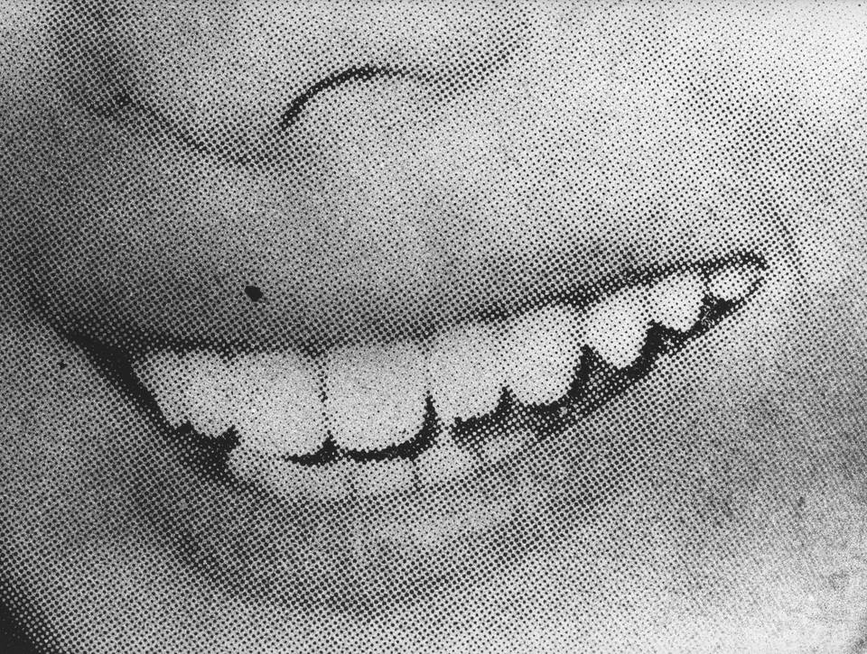 A woman&rsquo;s smile rendered in halftone printing dots — the teeth visible through mechanical reproduction noise.